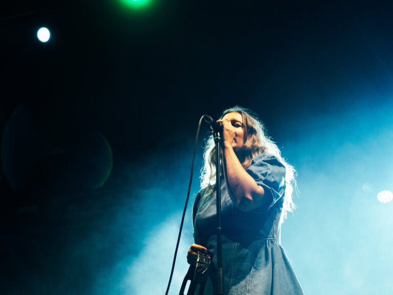 Nina de Juan cantando de pie agarrada al pie de micro bajo una luz azul en el Patio de la Diputación de Sevilla