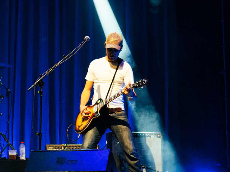 Paco López tocando la guitarra con luz azul y un amplificador Fender detrás en el concierto de Morgan en Sevilla