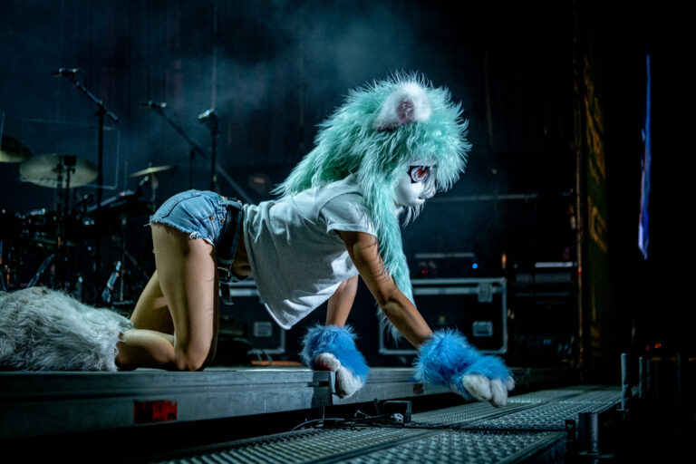 La bailarina con cabeza de peluche turquesa avanzando por la pasarela en el concierto de Ouineta