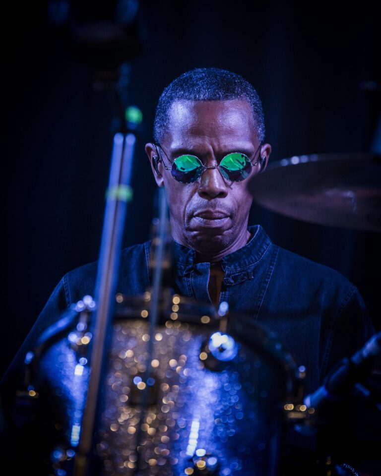Oscar Harrison tocando la batería con gafas redondas bajo luz azul en el concierto de Ocean Colour Scene en Sevilla