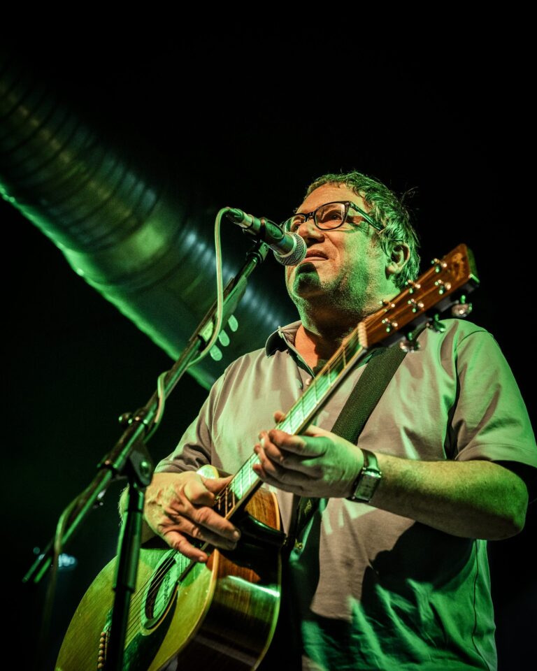 Simon Fowler tocando la guitarra acústica y cantando bajo luz verde en la Sala Custom de Sevilla