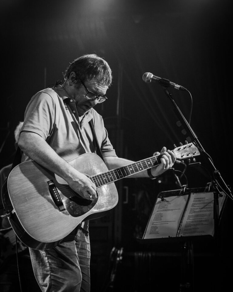 Simon Fowler tocando la guitarra acústica junto al atril en blanco y negro en el concierto de Ocean Colour Scene en Sevilla