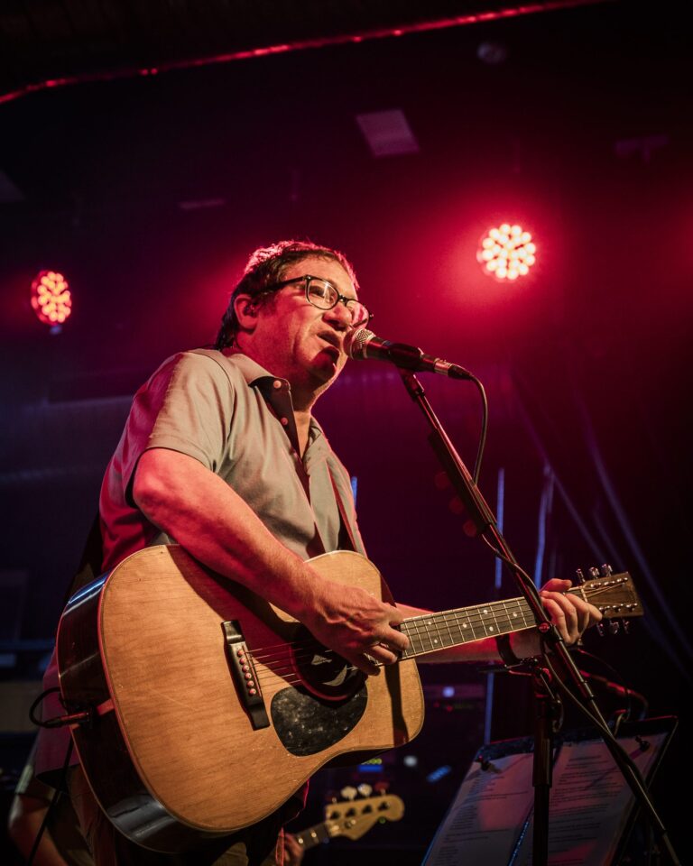 Simon Fowler cantando con su guitarra acústica bajo dos focos rojos en el concierto de Ocean Colour Scene en Sevilla