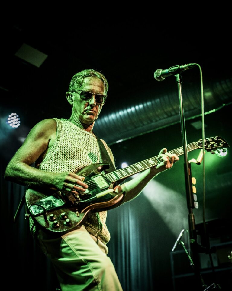 Steve Cradock tocando la guitarra eléctrica bajo luz verde frente a su micrófono en la Sala Custom de Sevilla